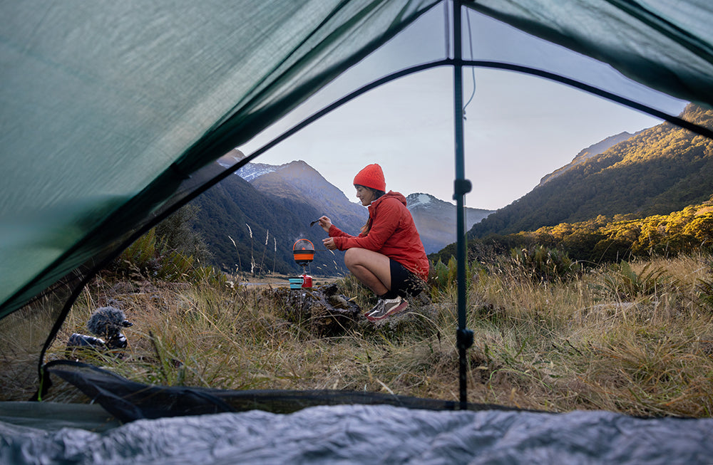 Outdoor Online Shop FluxPerfect, Frau mit Campingkocher in den Bergen