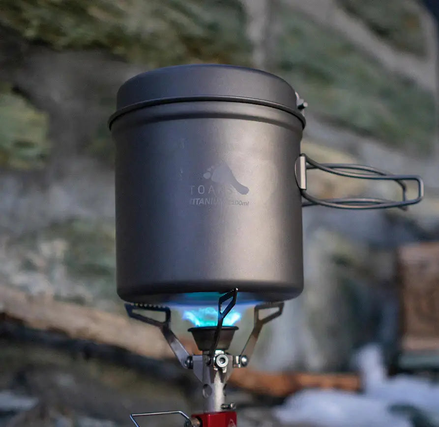 Hier sieht man das Kochset – TOAKS – Titanium Kochset aus Topf und Pfanne im Einsatz auf einem Gasherd - durch das Titanium ist es äußerst stabil und daher perfekt für jedes Outdoor Abenteuer