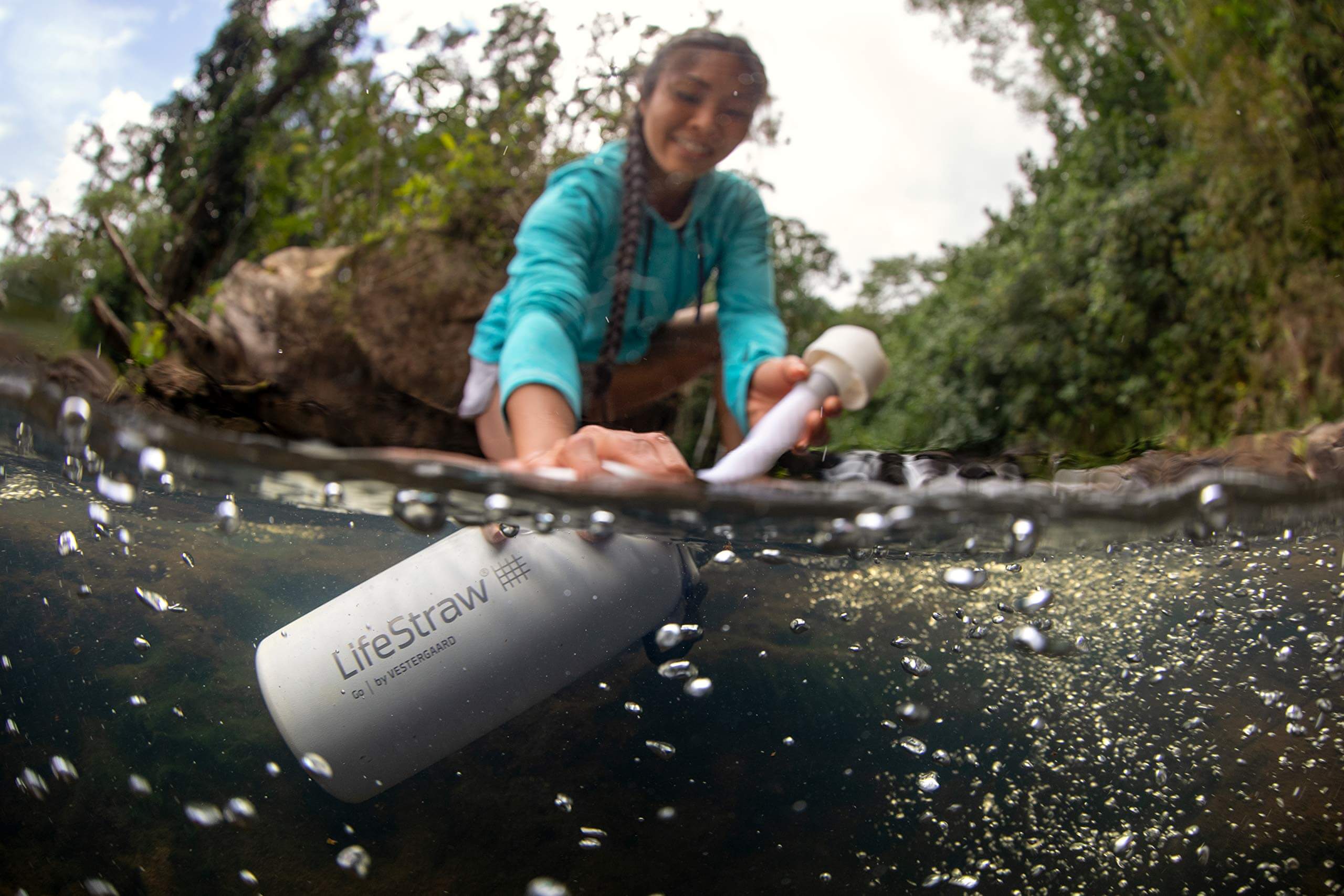 Eine Dame taucht ihren LifeStraw Go 1.0 in einen Bach um den Verwendungszweck als Outdoor Equipment ersichtlich zu machen